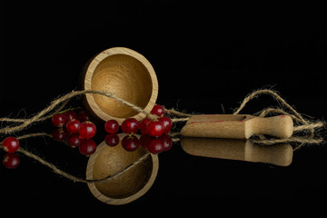 Lot of whole fresh red currant with wooden scoop in bamboo bowl with jute rope isolated on black glass