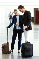 Two smiling young business partners using a smartphone at the airport