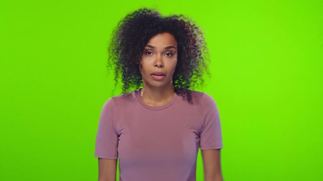 Pretty hesitant young dark-skinned female has clueless doubtful expression, shrugs shoulders throw her hands up with hesitation isolated over chroma key, doesnt know what to do. Hesitation concept