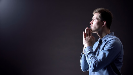 Young male praying, blessing God under light from heaven, Christianity sign