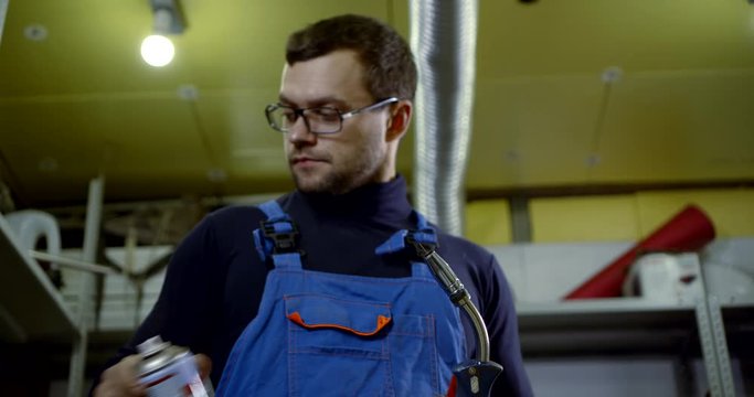 young man cleans welding machine with spray in workshop