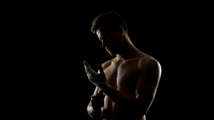 Fototapeta na wymiar Male boxer using hand wraps, protecting wrists from injuries before punching