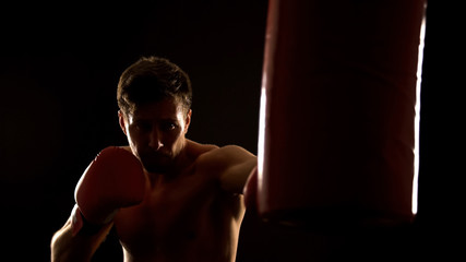 Male boxer punching boxing bag, warming up before competition, martial arts