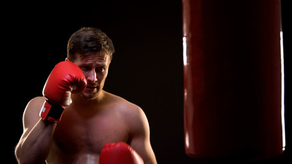 Sweaty sportsman training with boxing bag, fighting with insecurities concept