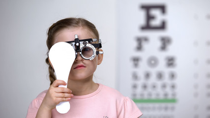 Child in special glasses with eye closed checking vision, astigmatism diagnosis - obrazy, fototapety, plakaty