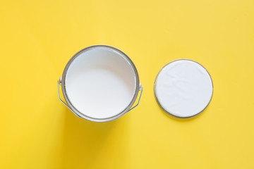 Open can of white paint on yellow background.