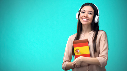 Girl listening Spanish audio lessons in headset, book in hands, translations