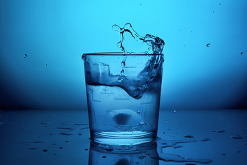 glass of water with splash on blue lighting background