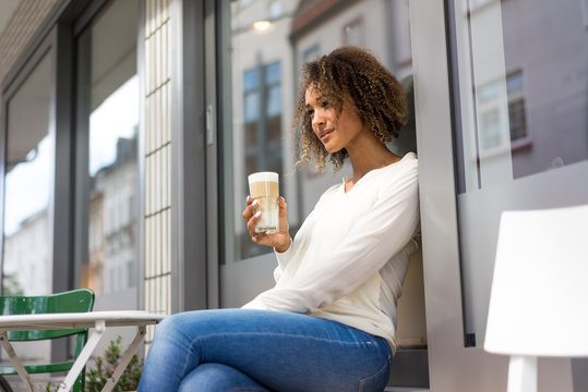 Young woman relaxing at pavement cafe with Latte Macchiato