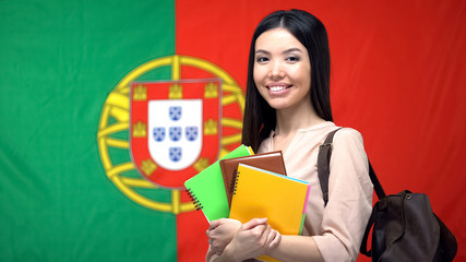 Asian female student holding copybooks against Portuguese flag background