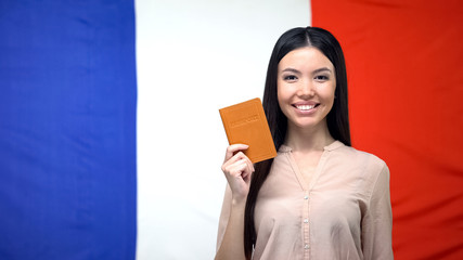 Smiling woman holding passport against French flag background, travel abroad