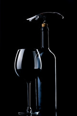 A bottle of wine. A glass filled with red wine. Natural cork. Metal corkscrew.