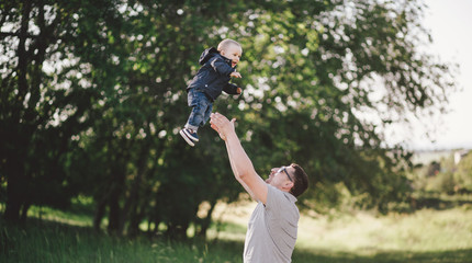 Happy father playing with his little son in a green park.