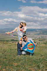 Happy family flying a colorful kite on green meadow.