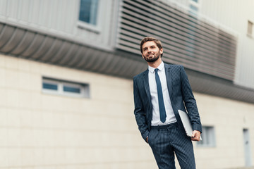 Businessman in suit with laptop in his hand goes to work on the road to the entrance of a glass office building.