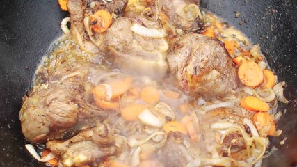Pieces of lamb with onion and carrots are fried in boiling oil on the fire. As a stage in the preparation of traditional pilaf. The process of cooking national food.