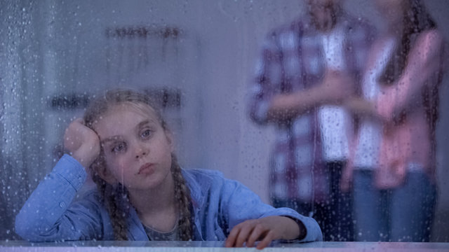 Unhappy little girl behind rainy window, foster parents coming to adopt child