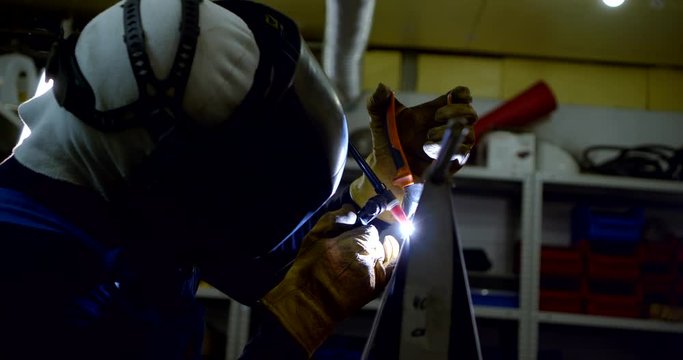 worker in protective mask welds metal construction in shop