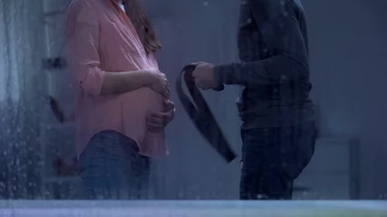 Deurstickers Man threatening pregnant woman with belt behind rainy window, family assault © motortion