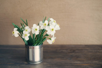 Narcissus flowers bouquet in the metal vase on a wooden surface, toned