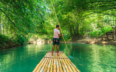 Man rowing bamboo raft, Martha Brae. Tourist boy whilst on cruise  on vacation in Montego Bay, Jamaica, Caribbean. - obrazy, fototapety, plakaty