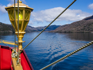 Lake and forests in Japan - picture taken from a boat on the lake, decorative gold coloured lantern, red hull and several lines of ropes in foreground