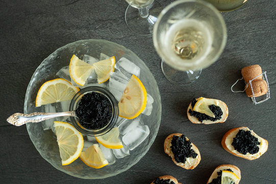 Sturgeon black caviar, sandwiches and champagne on black background