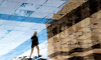 Blurry reflection shadow silhouettes of  a person  walking  on wet city street