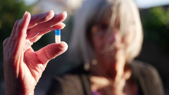 An old woman holding a prescription medication drug pill to improve her health and cure illness.