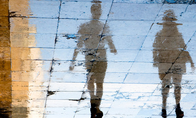 Blurry reflection shadow silhouettes of  a two people walking on a wet street  on a  summer day