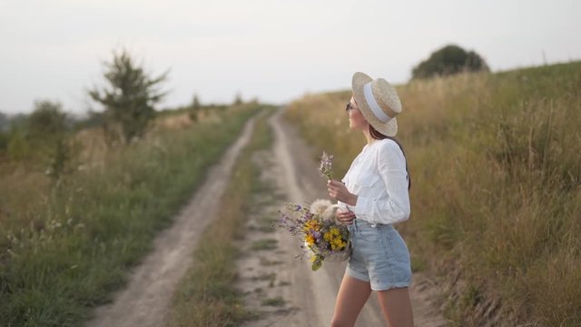 Young woman in a sunhat carrying flowers in the countryside