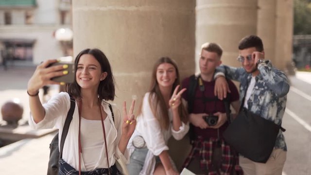 Four young friends are standing on a stairs of some ancient building and making a selfie. They are tourists cause they are hoding a map of the city.