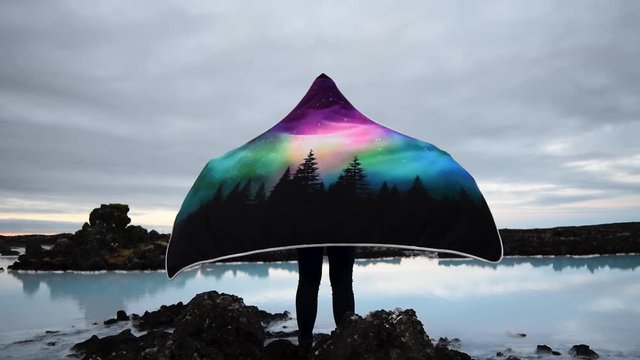 unrecognizable women with hooded blanket standing next to blue lagoon lake