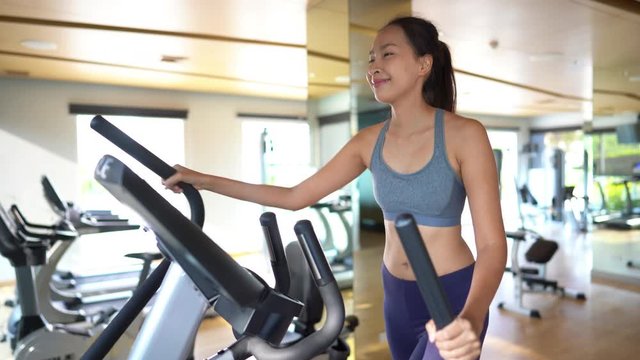 Young Asian woman working out in a resort gym on the elliptical machine.