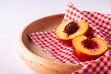 Two slice of peach nectarine fruit with seed in wooden plate with red checkered tablecloth on white background, copy space, angle view