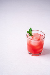 Fresh cold watermelon juice with ice cubes and green mint leaf in glass drink on white background, copy space, angle view