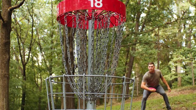 Man plays disc golf, makes putt, slow motion, hits center