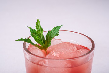 Fresh cold watermelon juice with ice cubes and green mint leaf in glass drink on white background, macro, selective focus