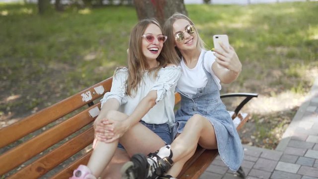 Two pretty girls sitting on park bench taking photos for social media