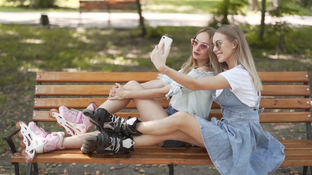 Girls having fun on warm day in park, rollerblading and talking photos with phone
