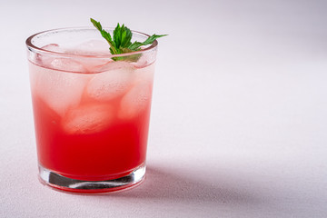 Fresh cold watermelon juice with ice cubes and green mint leaf in glass drink on white background, copy space, angle view