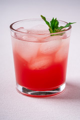 Fresh cold watermelon juice with ice cubes and green mint leaf in glass drink on white background, copy space, angle view