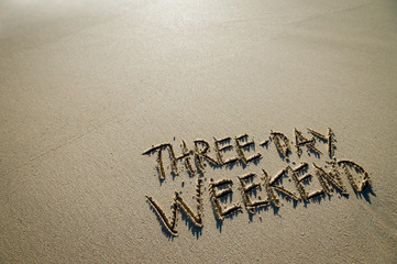 Three-Day Weekend message handwritten on the shore of a beach with smooth sand copy space