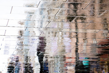 Blurry reflection shadow silhouettes of  people walking on a wet city street