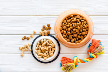 Dry dog food in bowl and toys on white wooden background top view copyspace