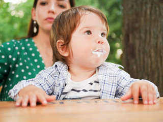 mom feeds her baby on the street. A mother feeds her little baby with a spoon on the street. mouth in food. healthy cottage cheese and yogurd