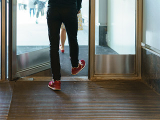 A photography of the feet of young man in red sneakers stepping out of an office door in summer...