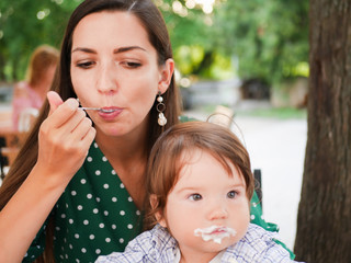 mom feeds her baby on the street. A mother feeds her little baby with a spoon on the street. mouth in food. healthy cottage cheese and yogurd