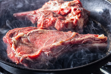 Smoke and steam rise from a beaf steak on grill pan.