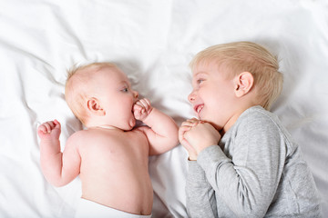 Cute baby and smiling older brother are lying on the bed. Play and interact. Top view